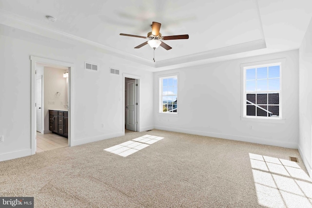 unfurnished bedroom featuring light carpet, a tray ceiling, visible vents, and baseboards