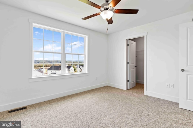 unfurnished bedroom featuring a spacious closet, ceiling fan, light carpet, baseboards, and visible vents