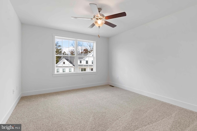 carpeted spare room with visible vents, a ceiling fan, and baseboards