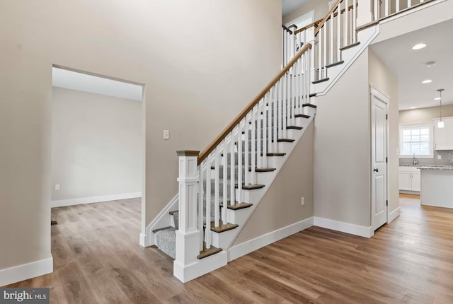 stairway with baseboards, wood finished floors, and recessed lighting