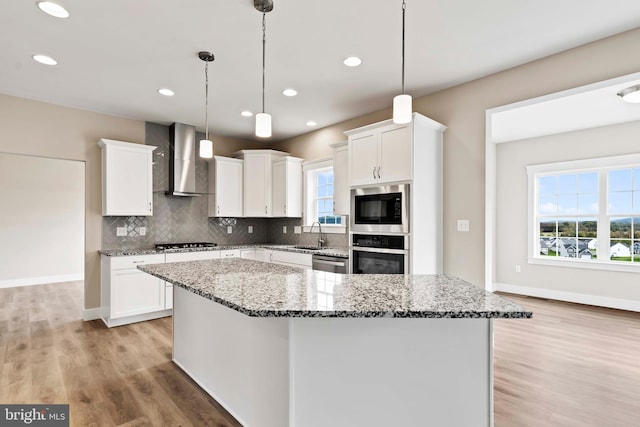 kitchen featuring wall chimney range hood, white cabinetry, stainless steel appliances, and a kitchen island