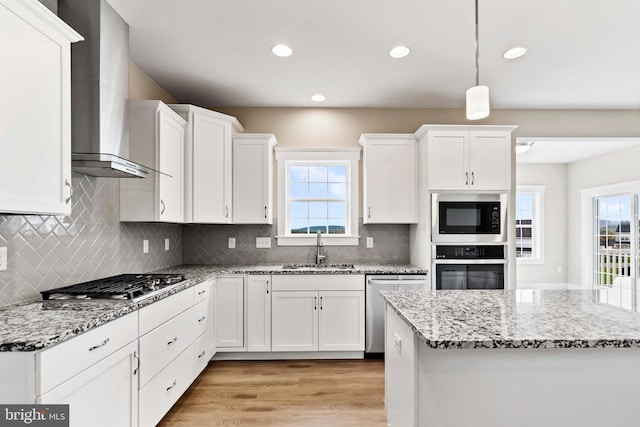 kitchen with white cabinets, wall chimney exhaust hood, appliances with stainless steel finishes, and a sink