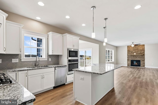 kitchen with a ceiling fan, tasteful backsplash, a sink, stainless steel appliances, and a fireplace