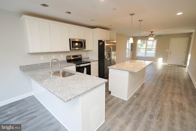 kitchen with appliances with stainless steel finishes, sink, kitchen peninsula, pendant lighting, and white cabinets