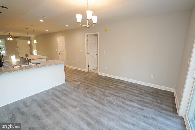 kitchen featuring light stone countertops, sink, ceiling fan with notable chandelier, decorative light fixtures, and dark wood-type flooring