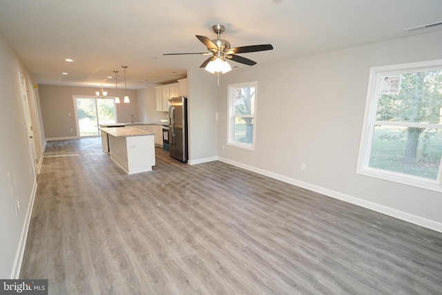 kitchen featuring white cabinets, a healthy amount of sunlight, stainless steel refrigerator, pendant lighting, and a center island