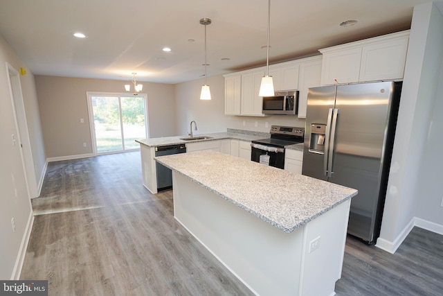 kitchen with appliances with stainless steel finishes, sink, kitchen peninsula, hanging light fixtures, and white cabinetry