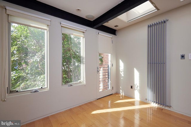 spare room featuring a wealth of natural light, beam ceiling, and light hardwood / wood-style floors