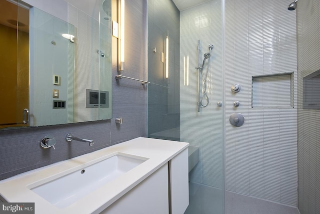 bathroom with vanity, a tile shower, backsplash, and tile walls