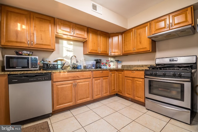 kitchen with dark stone countertops, stainless steel appliances, and light tile patterned floors