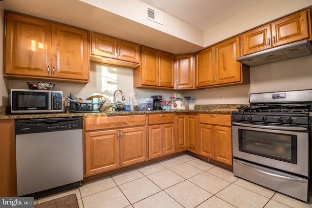 kitchen featuring sink, dark stone counters, stainless steel appliances, and light tile patterned floors