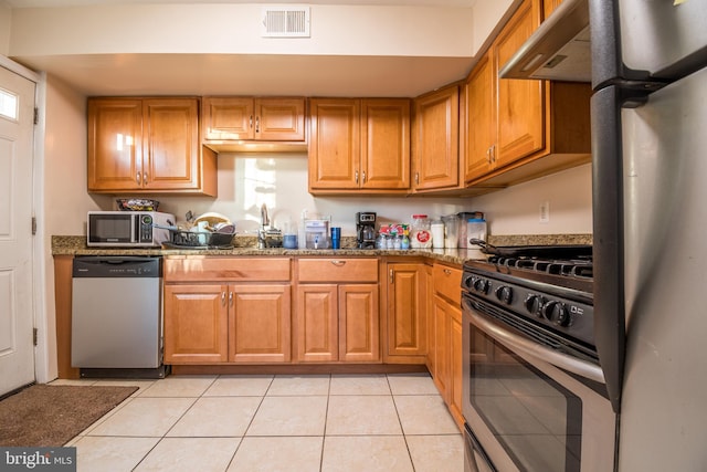 kitchen with appliances with stainless steel finishes, light tile patterned flooring, and dark stone counters