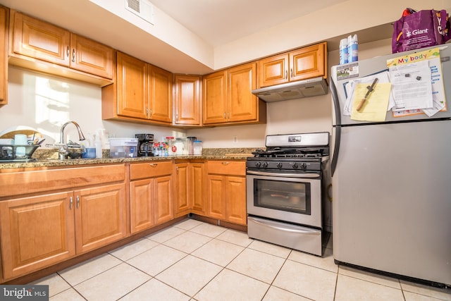 kitchen with dark stone countertops, stainless steel appliances, light tile patterned flooring, and sink