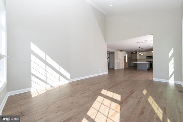 unfurnished living room featuring an inviting chandelier, hardwood / wood-style flooring, and a high ceiling