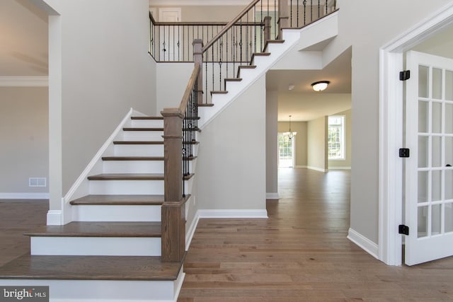 stairs with an inviting chandelier, ornamental molding, and wood-type flooring