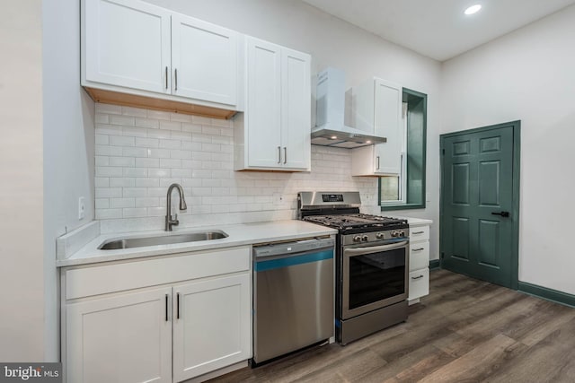 kitchen with wall chimney range hood, dark wood-type flooring, sink, white cabinetry, and appliances with stainless steel finishes