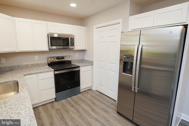 kitchen featuring light stone countertops, appliances with stainless steel finishes, light wood-type flooring, and white cabinets