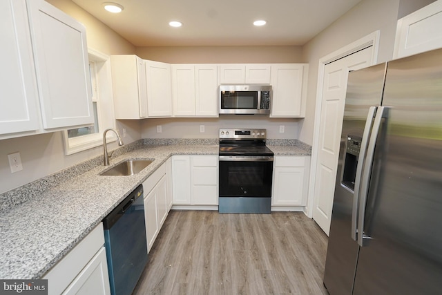 kitchen featuring sink, light stone countertops, white cabinetry, appliances with stainless steel finishes, and light hardwood / wood-style floors