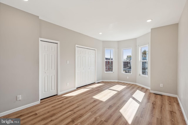 unfurnished bedroom with light hardwood / wood-style floors and two closets