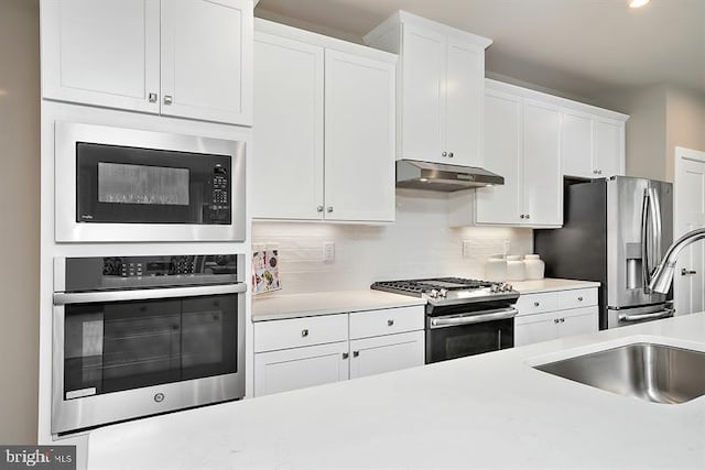 kitchen with appliances with stainless steel finishes, white cabinetry, sink, and backsplash