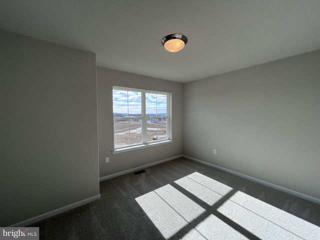 unfurnished room with visible vents, dark carpet, and baseboards