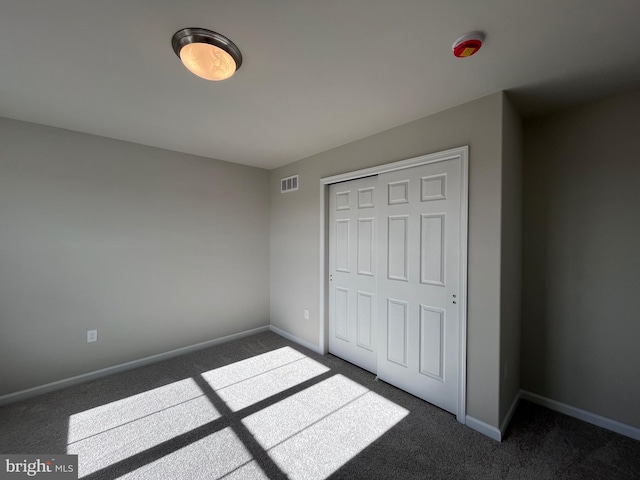 unfurnished bedroom featuring dark colored carpet, visible vents, baseboards, and a closet