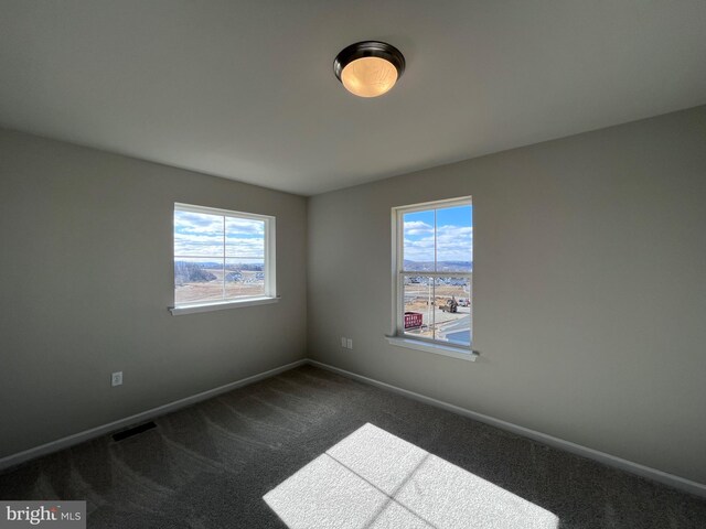 empty room featuring baseboards, visible vents, and dark carpet