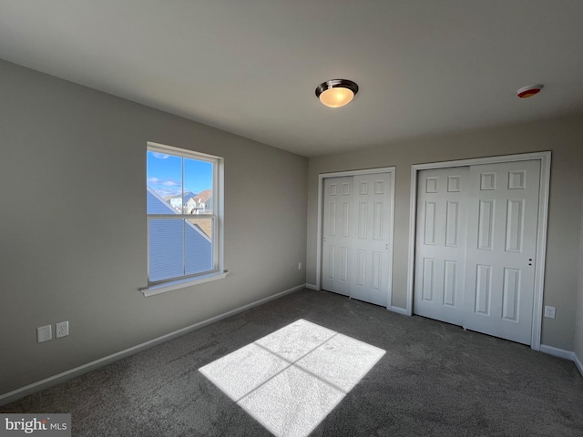 unfurnished bedroom featuring baseboards, multiple closets, and dark carpet