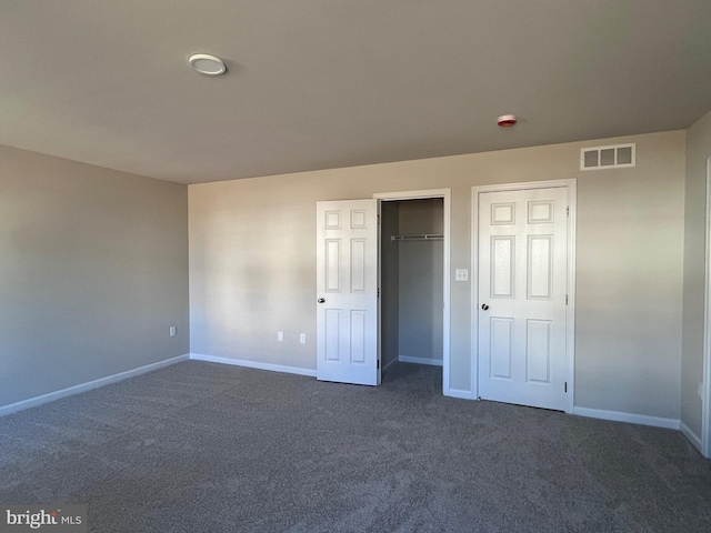 unfurnished bedroom with a closet, visible vents, baseboards, and dark colored carpet