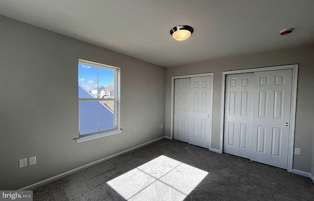 unfurnished bedroom featuring baseboards, multiple closets, and dark colored carpet