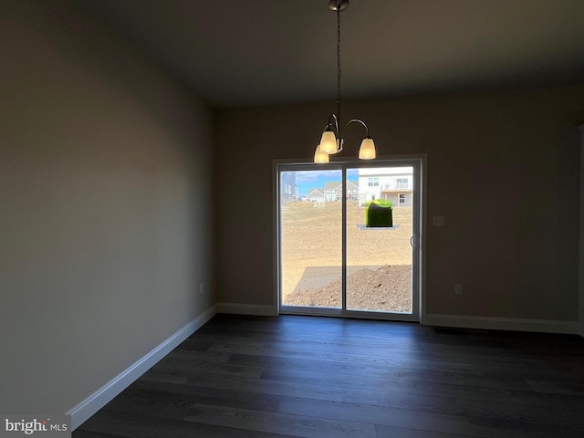 spare room with dark wood finished floors, a notable chandelier, and baseboards