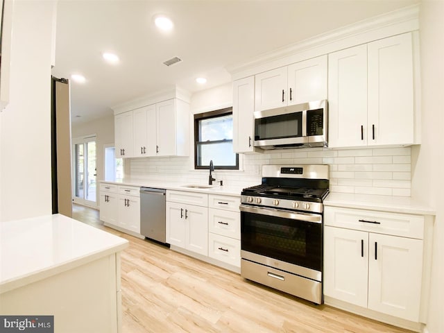 kitchen featuring sink, white cabinets, light wood-type flooring, appliances with stainless steel finishes, and tasteful backsplash