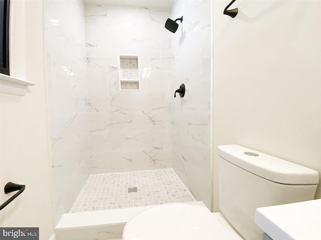 bathroom featuring a tile shower, toilet, and vanity