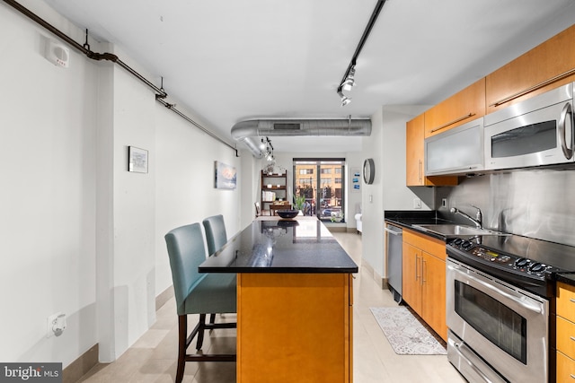 kitchen with a kitchen island, a breakfast bar area, stainless steel appliances, sink, and rail lighting