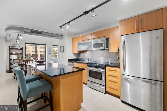 kitchen featuring backsplash, appliances with stainless steel finishes, a kitchen bar, sink, and a center island