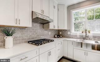 kitchen with stainless steel gas cooktop, white cabinets, sink, and backsplash