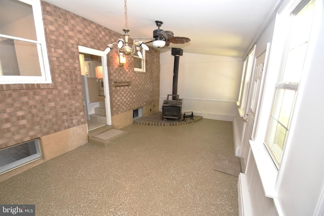 unfurnished living room with a wood stove, lofted ceiling, and ceiling fan with notable chandelier