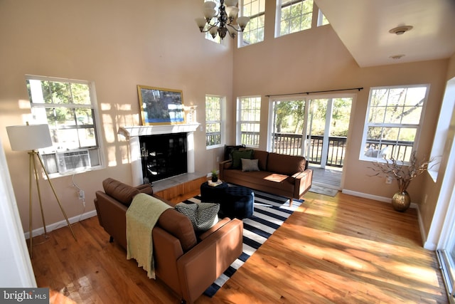 living room featuring an inviting chandelier, a high ceiling, a fireplace, and light hardwood / wood-style floors