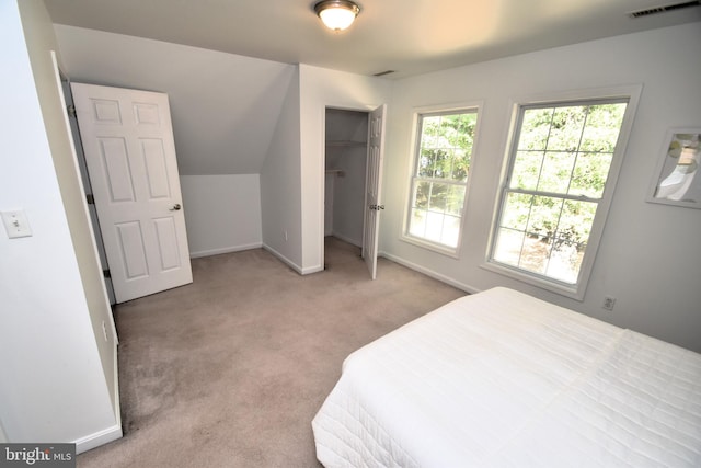 bedroom with a closet, light colored carpet, vaulted ceiling, and a walk in closet