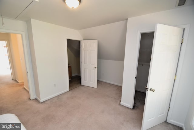 unfurnished bedroom with a spacious closet, vaulted ceiling, light colored carpet, and a closet