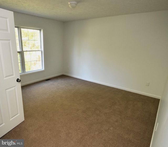 unfurnished room with a textured ceiling and dark carpet