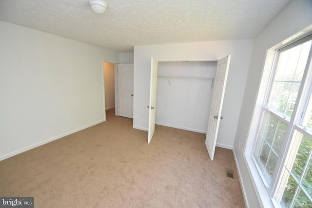 unfurnished bedroom with a textured ceiling, light colored carpet, and a closet