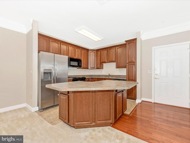 kitchen featuring light wood-type flooring, crown molding, black appliances, and a kitchen island