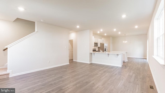 unfurnished living room featuring baseboards, an inviting chandelier, recessed lighting, light wood-style floors, and stairway