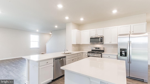 kitchen with stainless steel appliances, light countertops, wood finished floors, a sink, and a peninsula