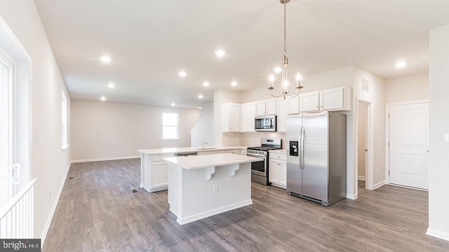 kitchen with hardwood / wood-style flooring, hanging light fixtures, a center island, white cabinets, and appliances with stainless steel finishes