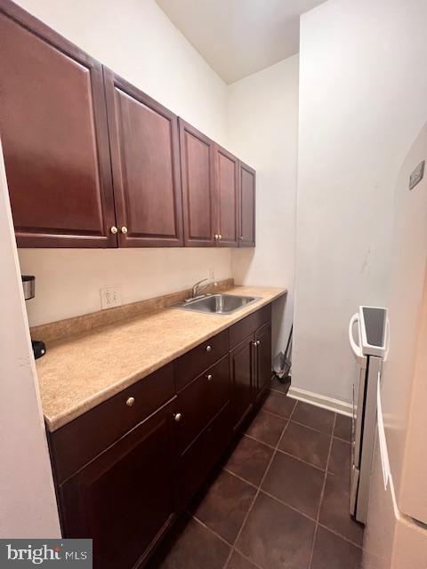 laundry room with dark tile patterned flooring, cabinets, and sink