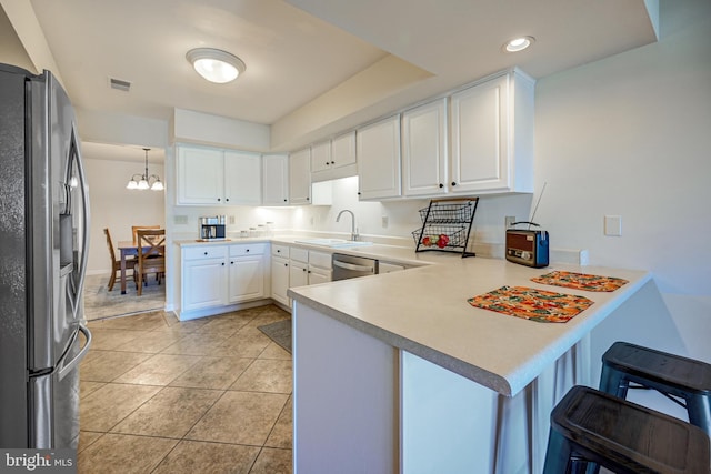 kitchen with appliances with stainless steel finishes, kitchen peninsula, a kitchen breakfast bar, decorative light fixtures, and white cabinets