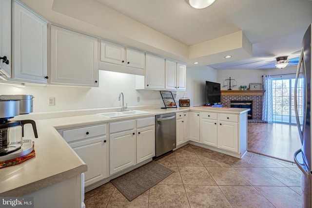 kitchen with kitchen peninsula, stainless steel appliances, sink, white cabinetry, and a fireplace