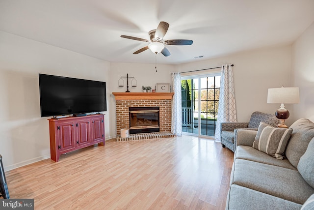 living room with a fireplace, light wood-type flooring, and ceiling fan